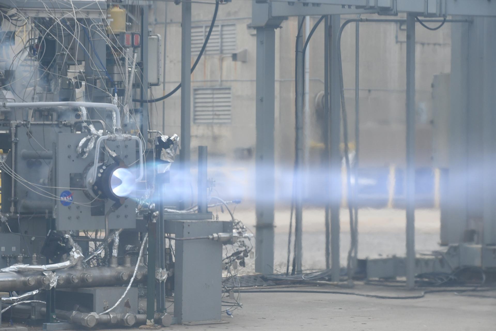 A rotating detonation rocket engine firing on a test stand, exhaust plume glowing blue